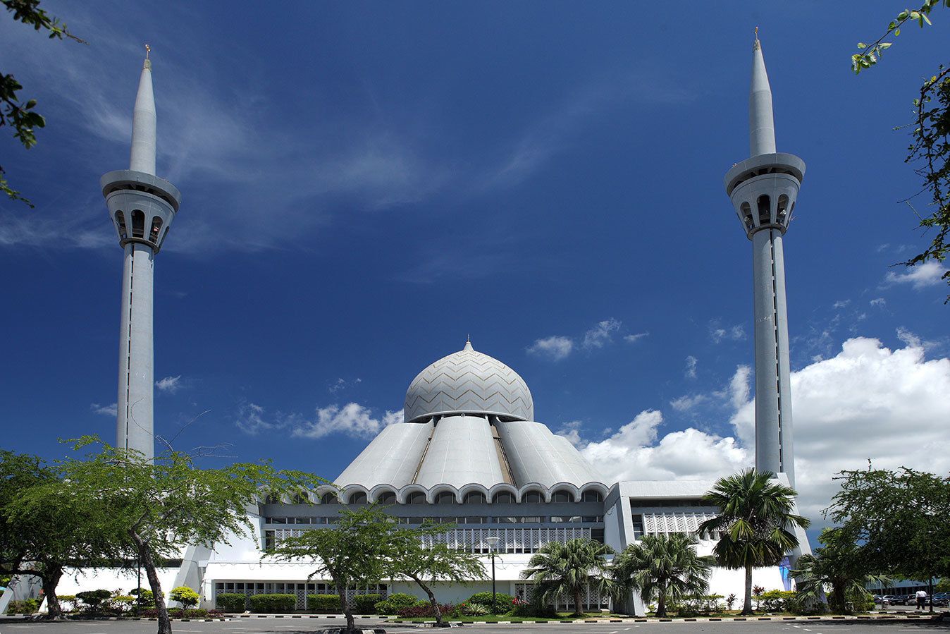 En moské med två minareter och en stor kupol, omgiven av träd och en klar himmel.