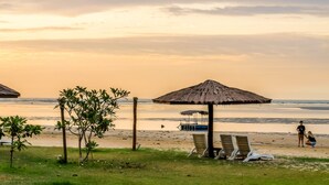 A beach with thatched umbrellas, lounge chairs, and a boat in the background.