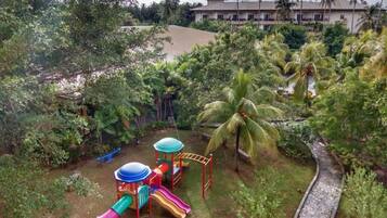 Explore a lush playground surrounded by greenery and palm trees, adjacent to a multi-story building with accessible pathways.