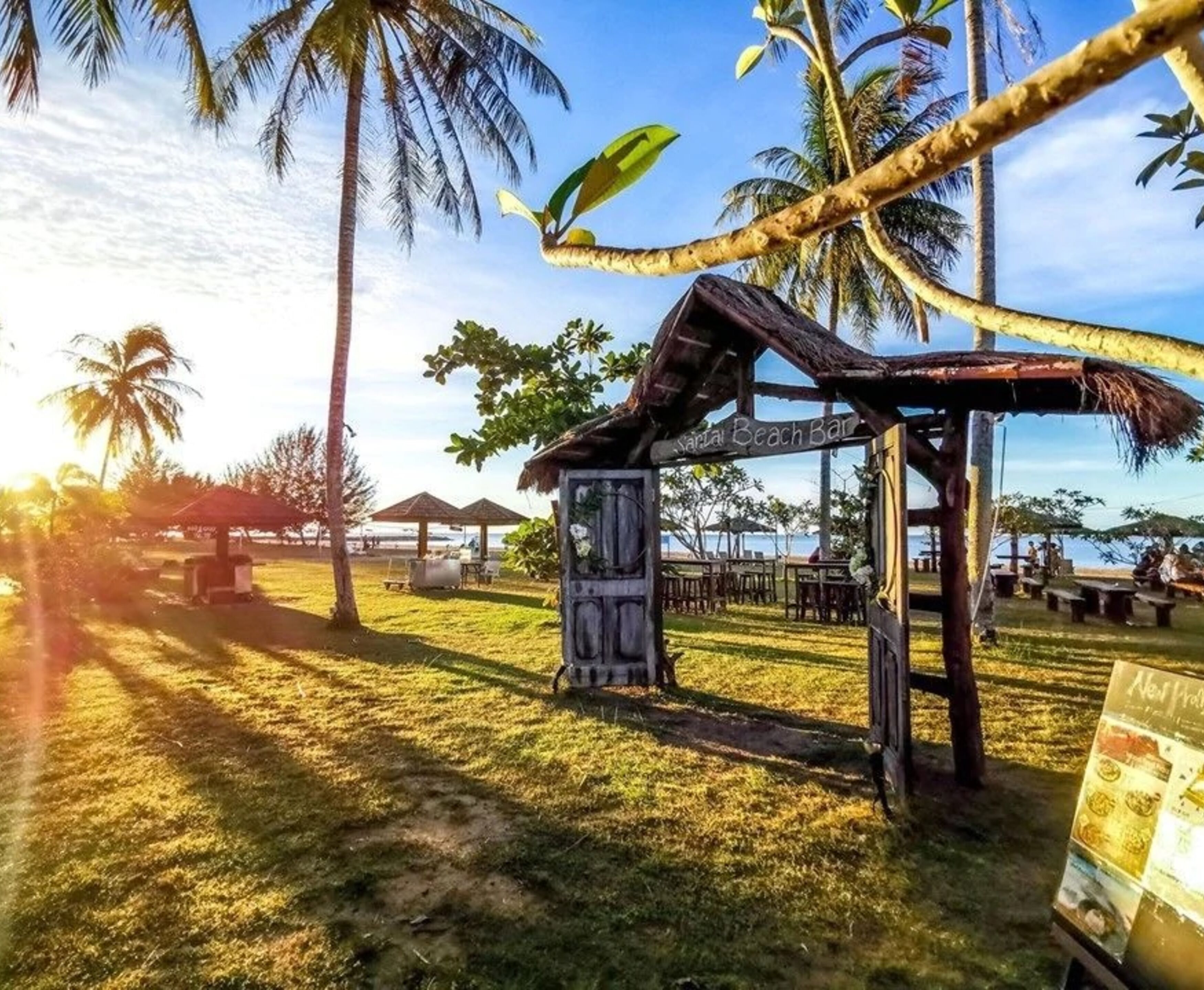 A beach bar with a thatched roof, surrounded by palm trees and beach chairs.