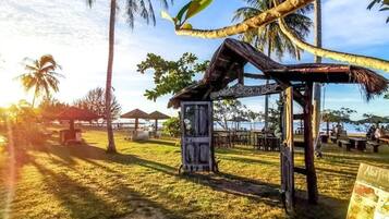 A beach bar with a thatched roof, surrounded by palm trees and beach chairs.