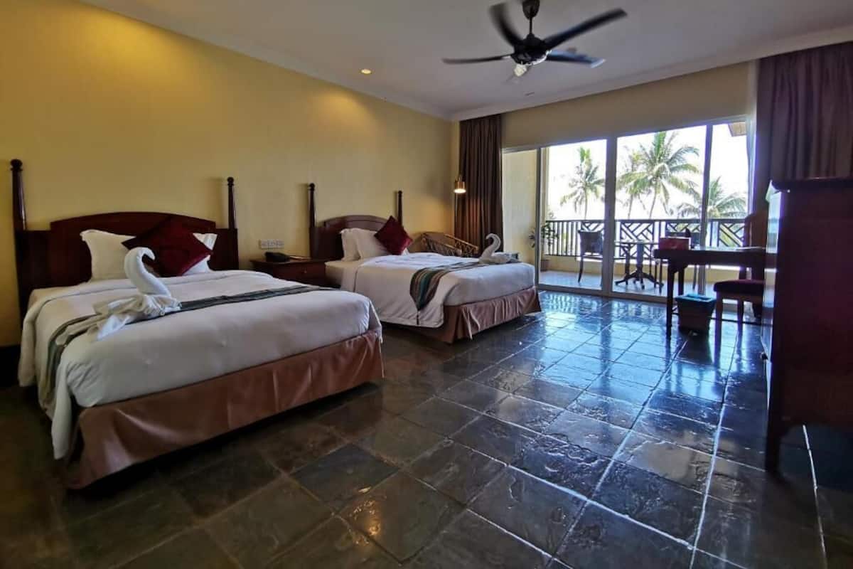 A hotel room with two beds, a ceiling fan, and a balcony with a view of palm trees.