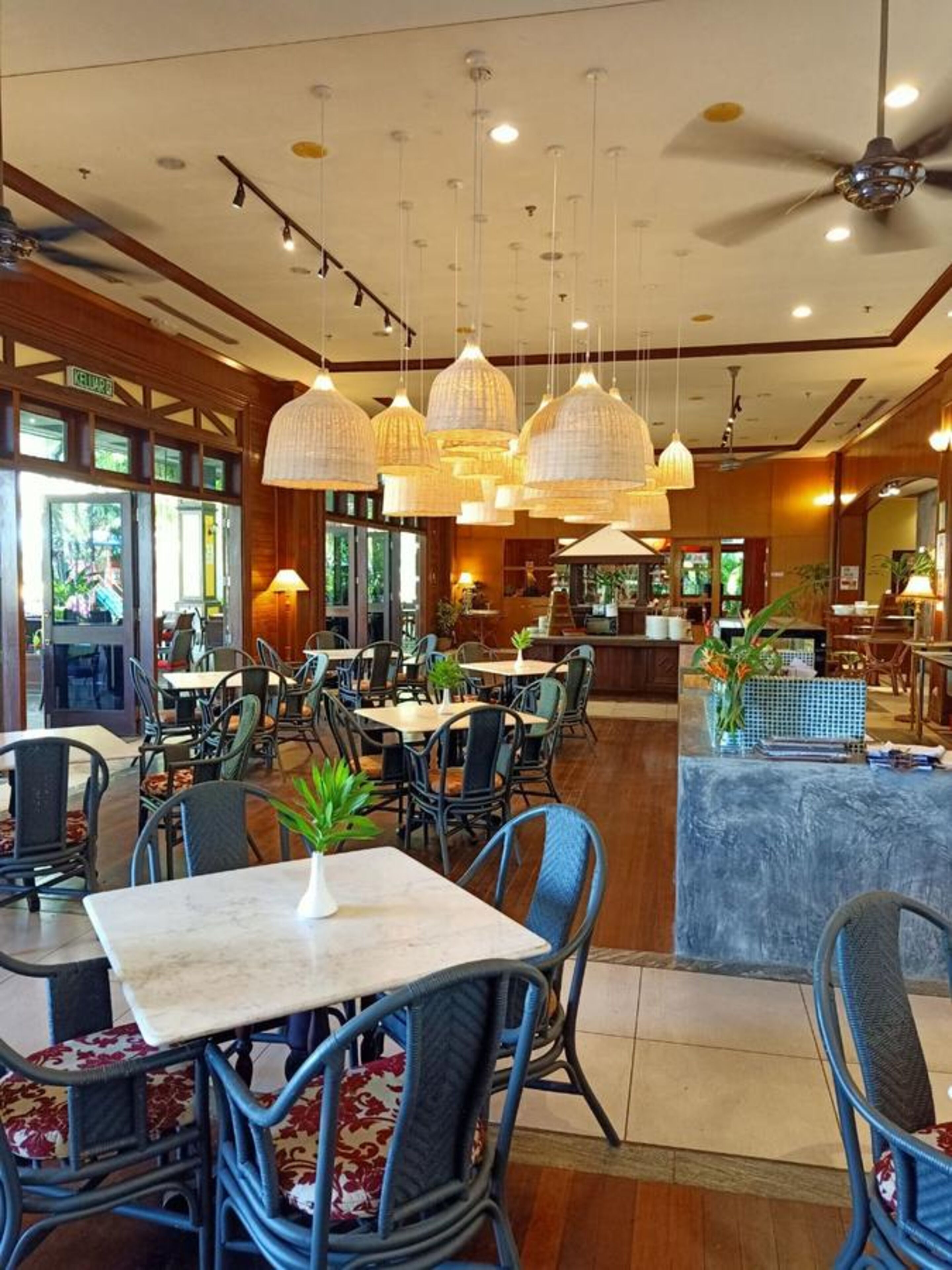Un restaurant doté de nombreuses tables et chaises, de luminaires suspendus et d’un ventilateur de plafond.