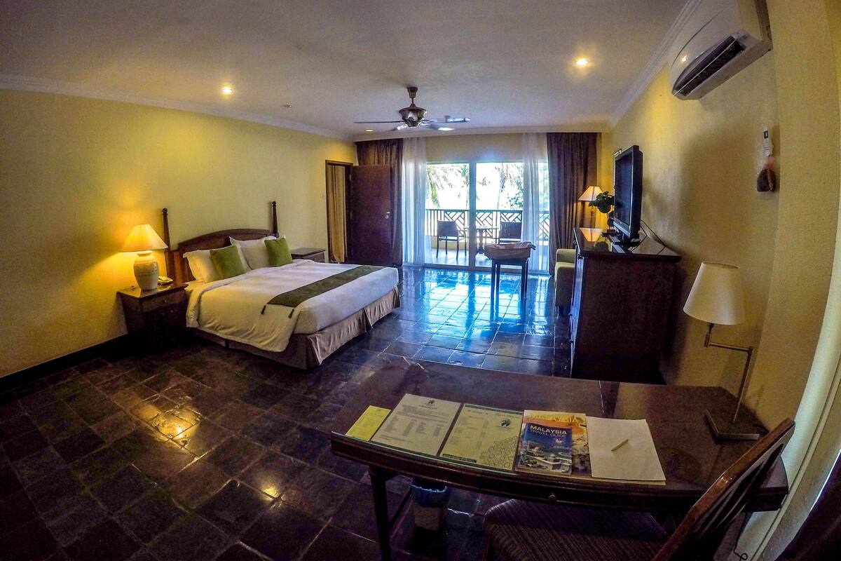 A hotel room with a bed, bedside table, desk, and a view of the outside.