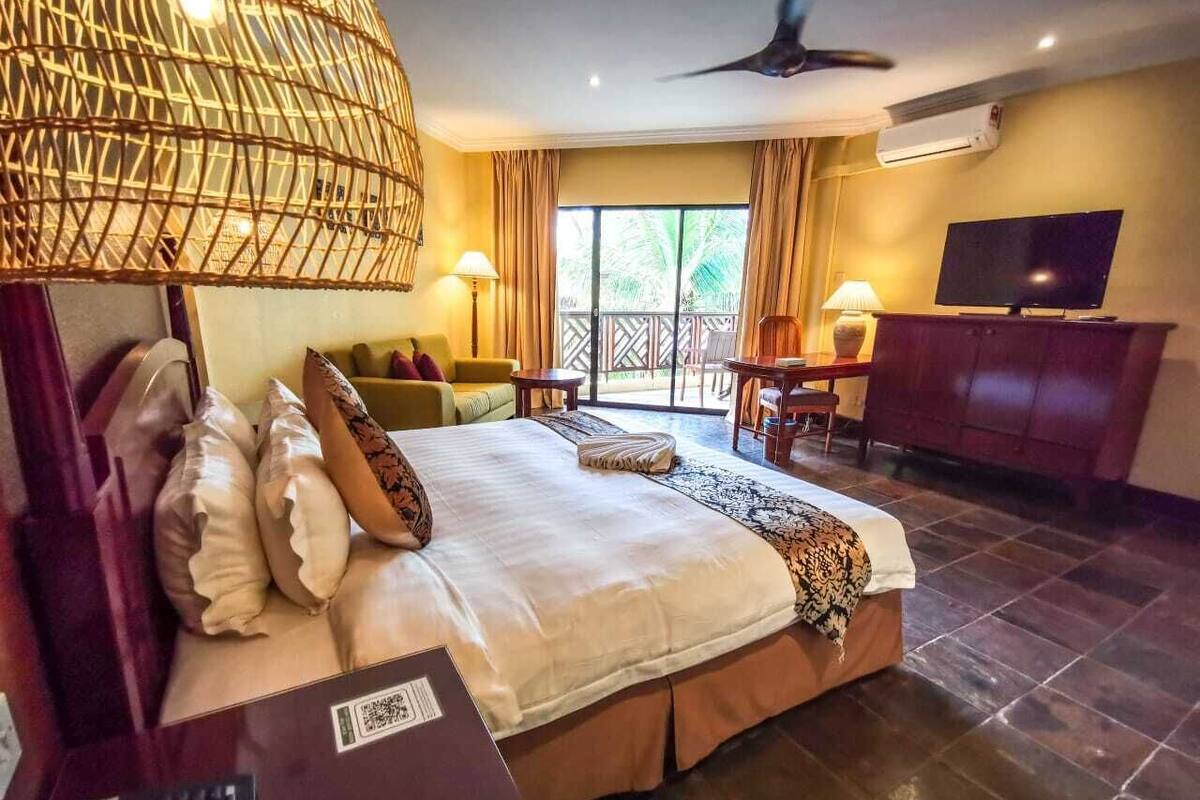 A hotel room with a large bed, a TV, a desk, and a balcony with a view.