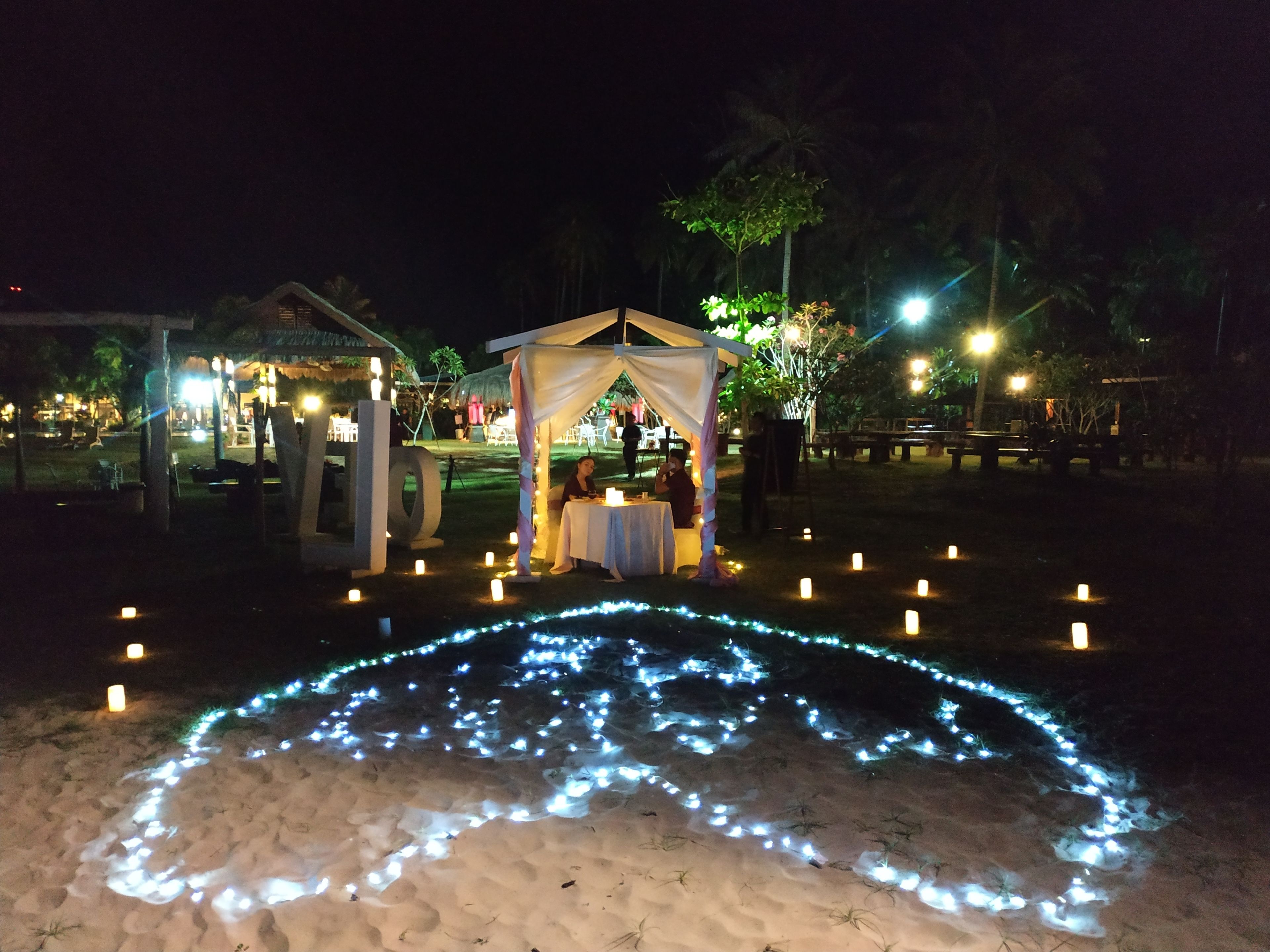 A tented outdoor area with a table and chairs, surrounded by candles and string lights on the ground.