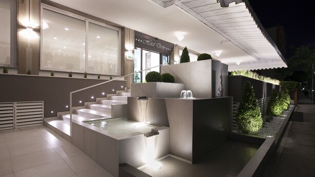Una entrada de hotel moderna con fachada de vidrio, una escalera que conduce a la entrada y un pequeño elemento decorativo de agua a la base de la escalera.