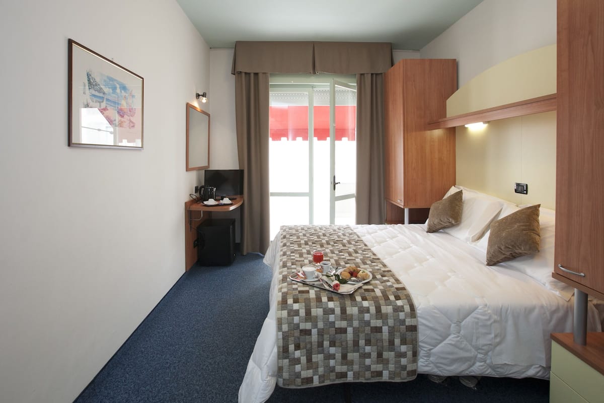 Habitación de hotel con cama, escritorio con silla, televisor y bandeja de desayuno sobre la cama.