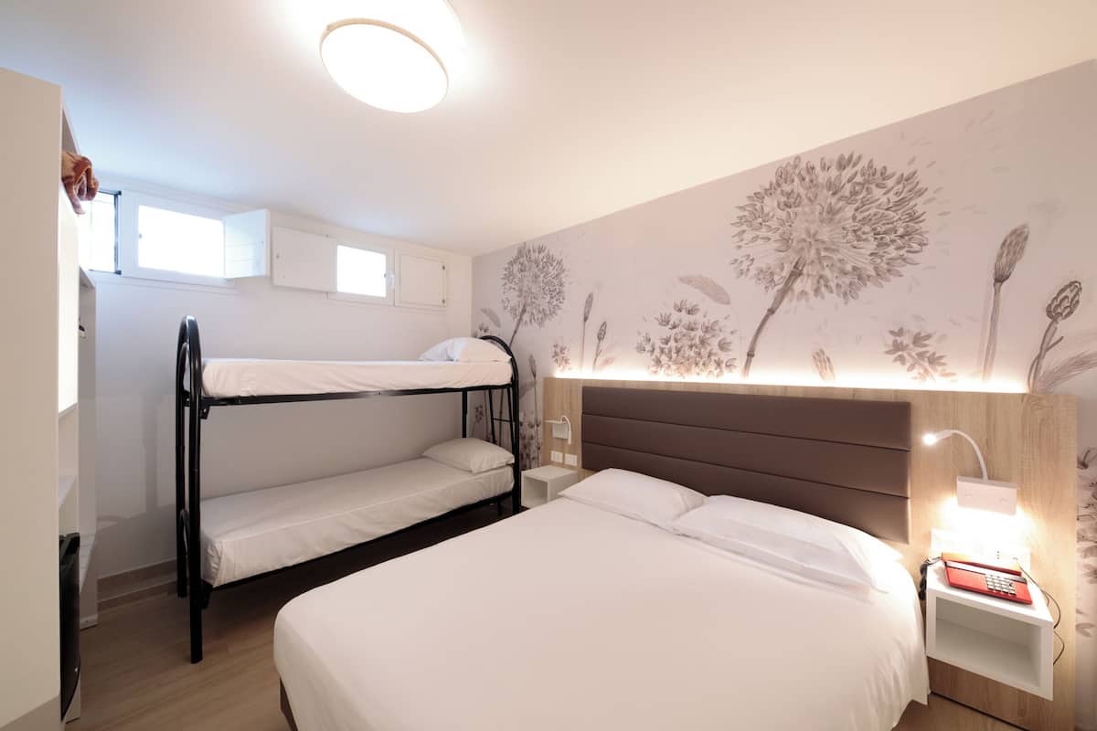 Una habitación con literas, una mesita de noche con lámpara y un papel tapiz floral en la pared.