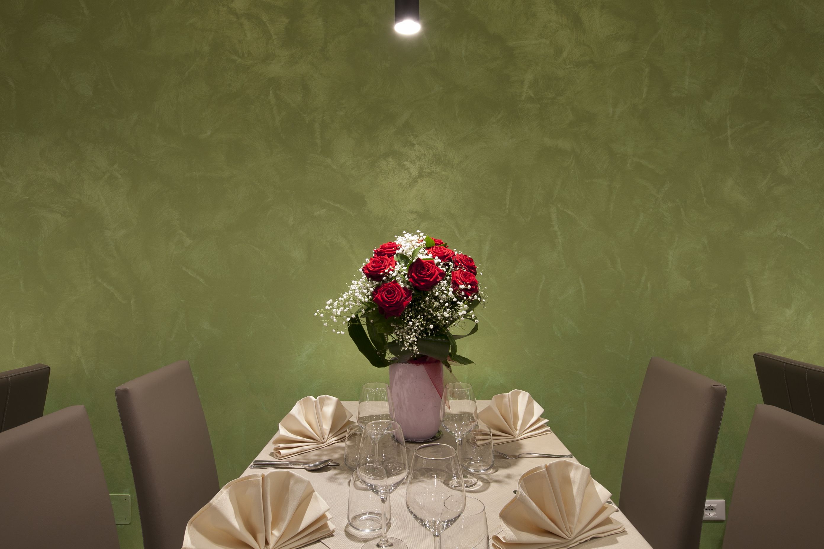 A dining table set with a vase of red roses and white flowers, surrounded by chairs and empty wine glasses.
