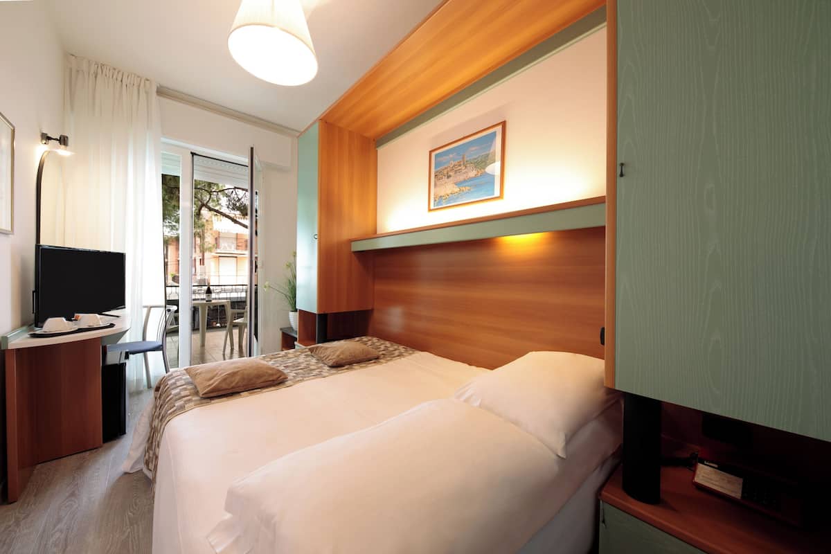 Habitación de hotel con dos camas, un escritorio con televisor y un cuadro en la pared.