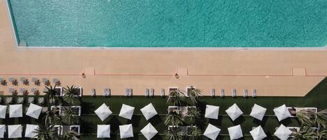 Vista aérea de una playa con piscina, filas de tumbonas y sombrillas.