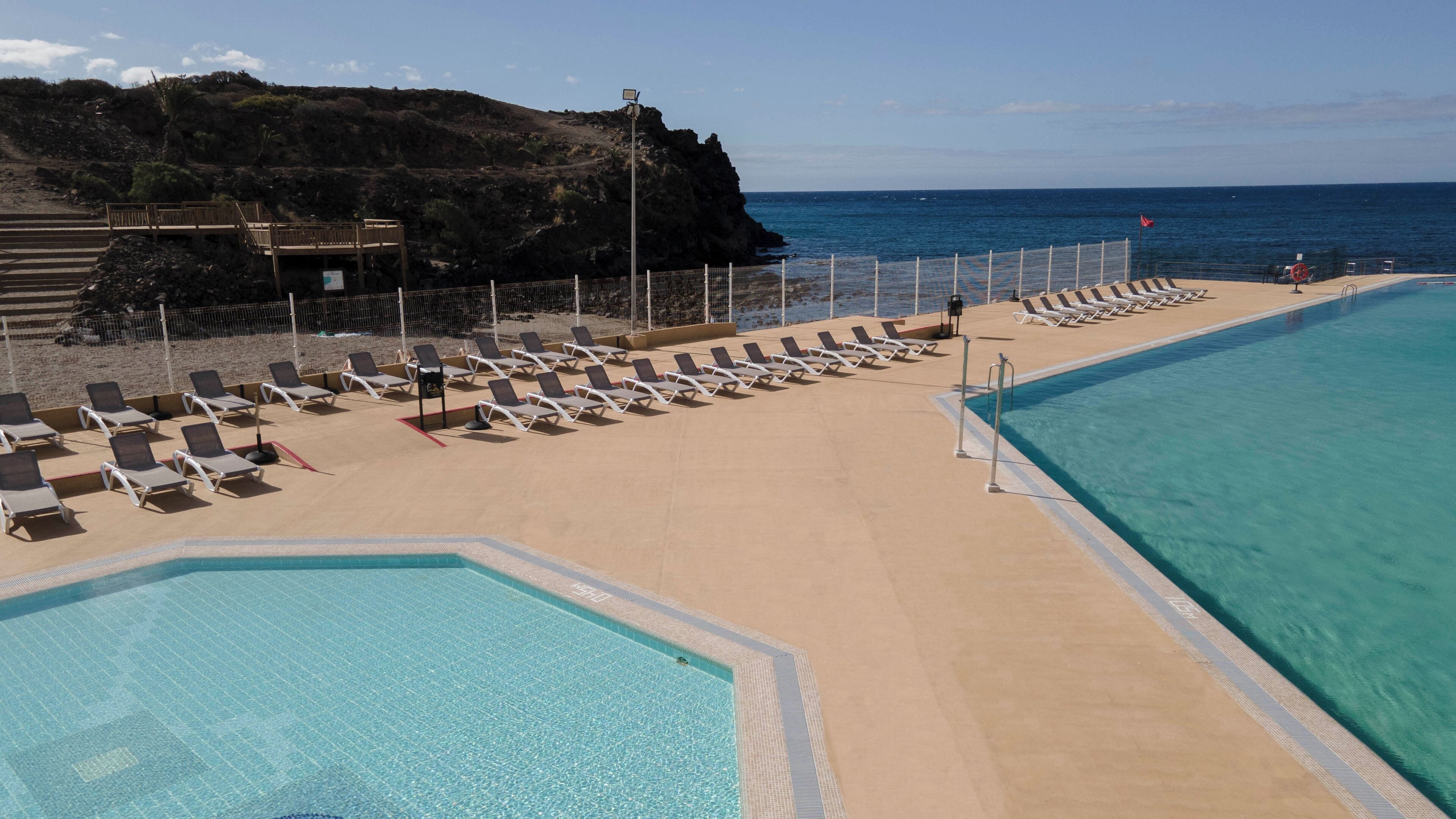 A poolside area with lounge chairs and a view of the ocean.