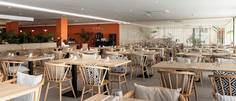 A spacious restaurant with multiple tables and chairs, a kitchen area, and a seating area with a view of the outdoors.