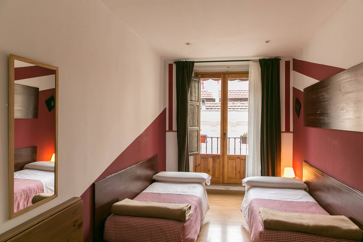 Habitación de hotel con dos camas, cabecera de madera, un espejo y un balcón con vistas.