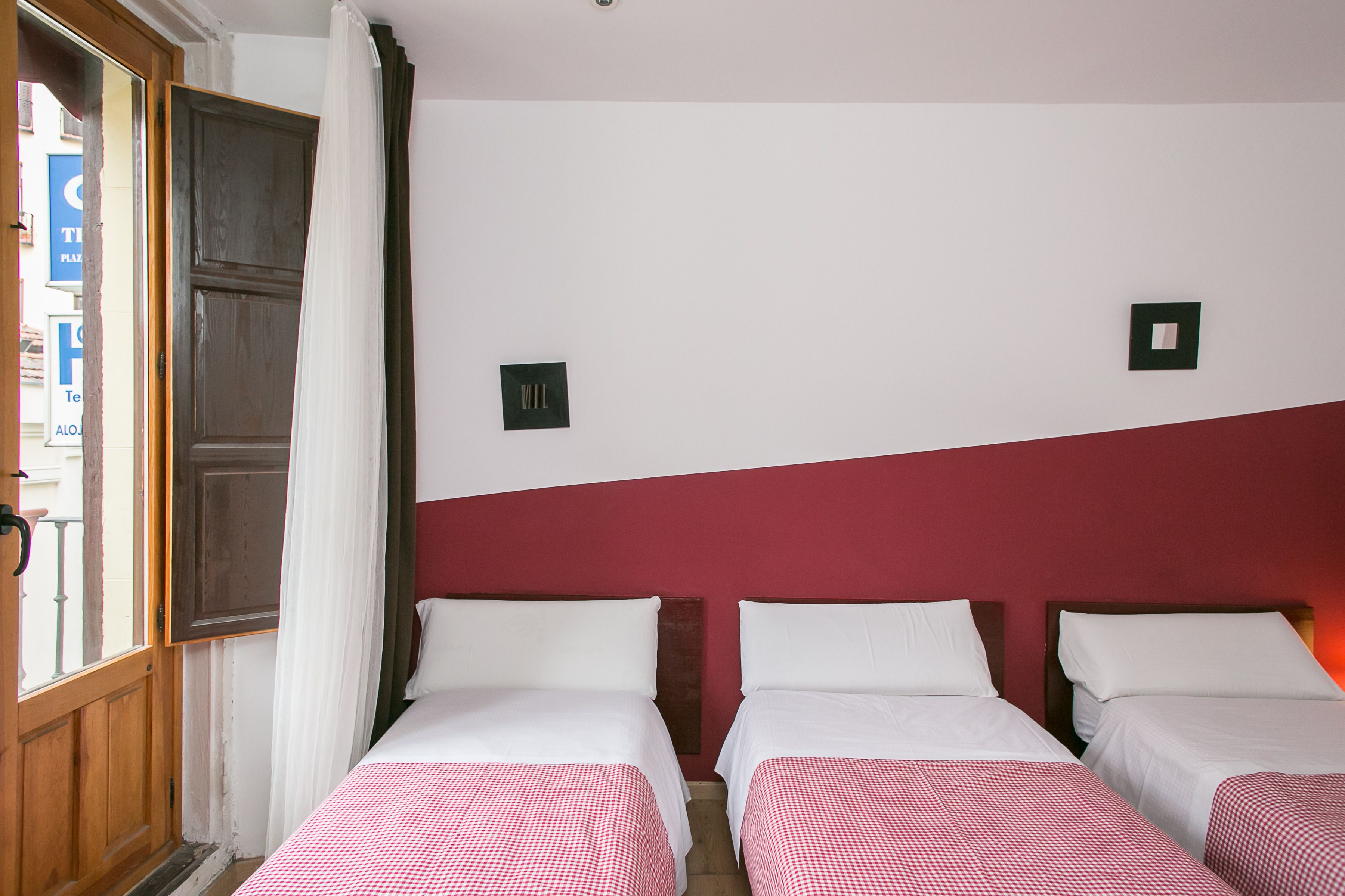 Habitación de hotel con dos camas, una puerta de madera y una pared de acento roja.