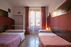 Habitación de hotel con dos camas, cabecera de madera, ventana con cortinas traslúcidas, lámpara de noche y repisa con un florero.