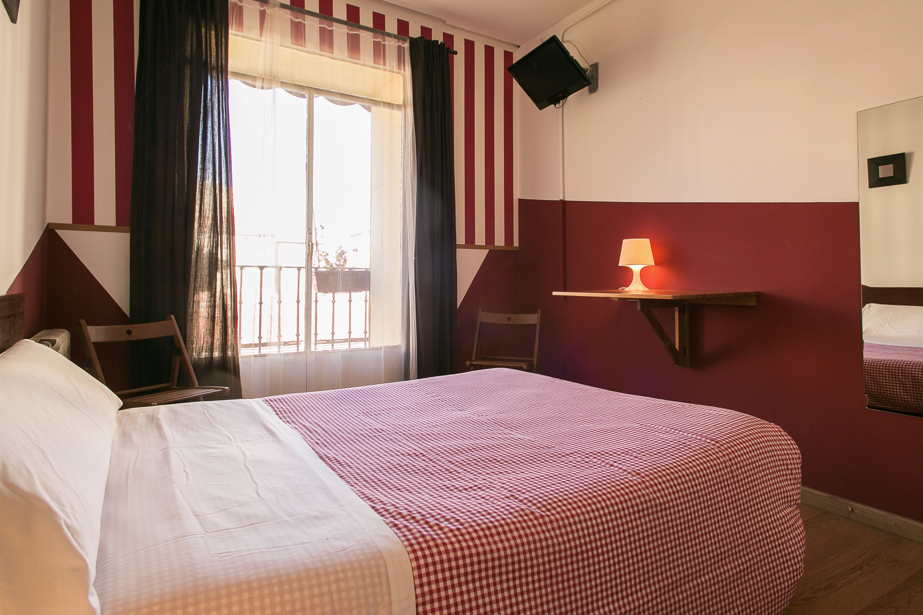Habitación de hotel con una cama grande, una ventana con cortinas, una mesita de noche con lámpara y un estante pequeño.