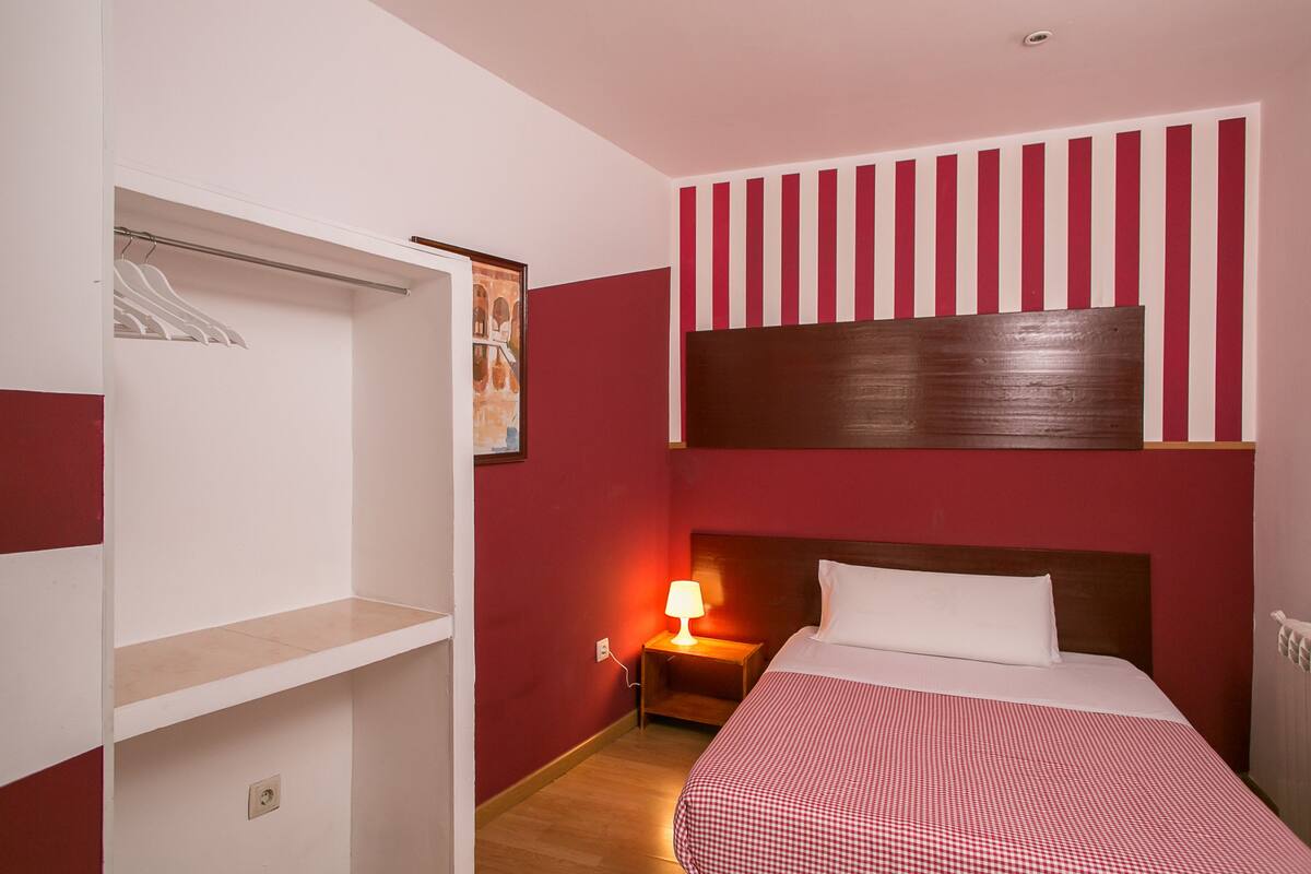 Una habitación de hotel con una cama, una mesita de noche con lámpara, un armario y un diseño de pared a rayas rojas y blancas.