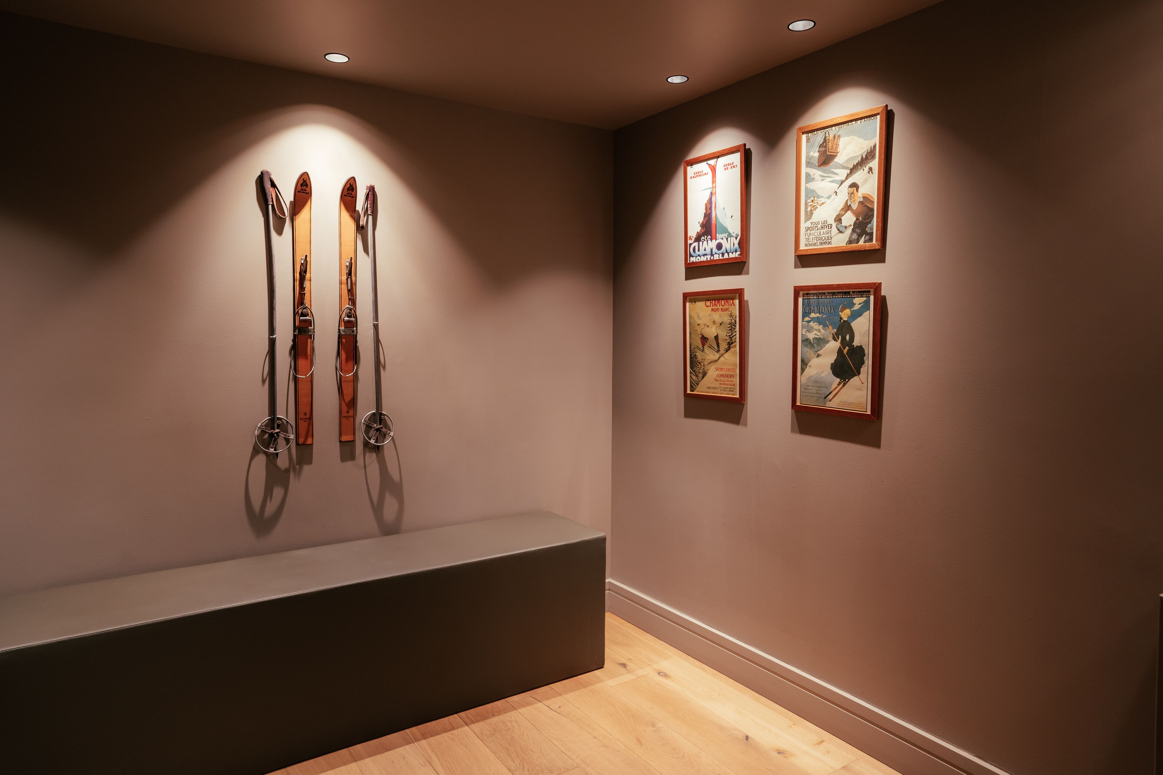 Une pièce avec un banc, des paires de skis appuyés contre le mur et trois tableaux encadrés.