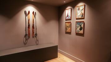 Une pièce avec un banc, des paires de skis appuyés contre le mur et trois tableaux encadrés.