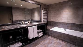 A modern bathroom with a large mirror, two sinks, a bathtub, and a towel rack.