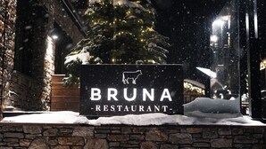 A sign for Bruna Restaurant with a snow-covered ground and a Christmas tree in the background. - Serras Andorra (Soldeu)