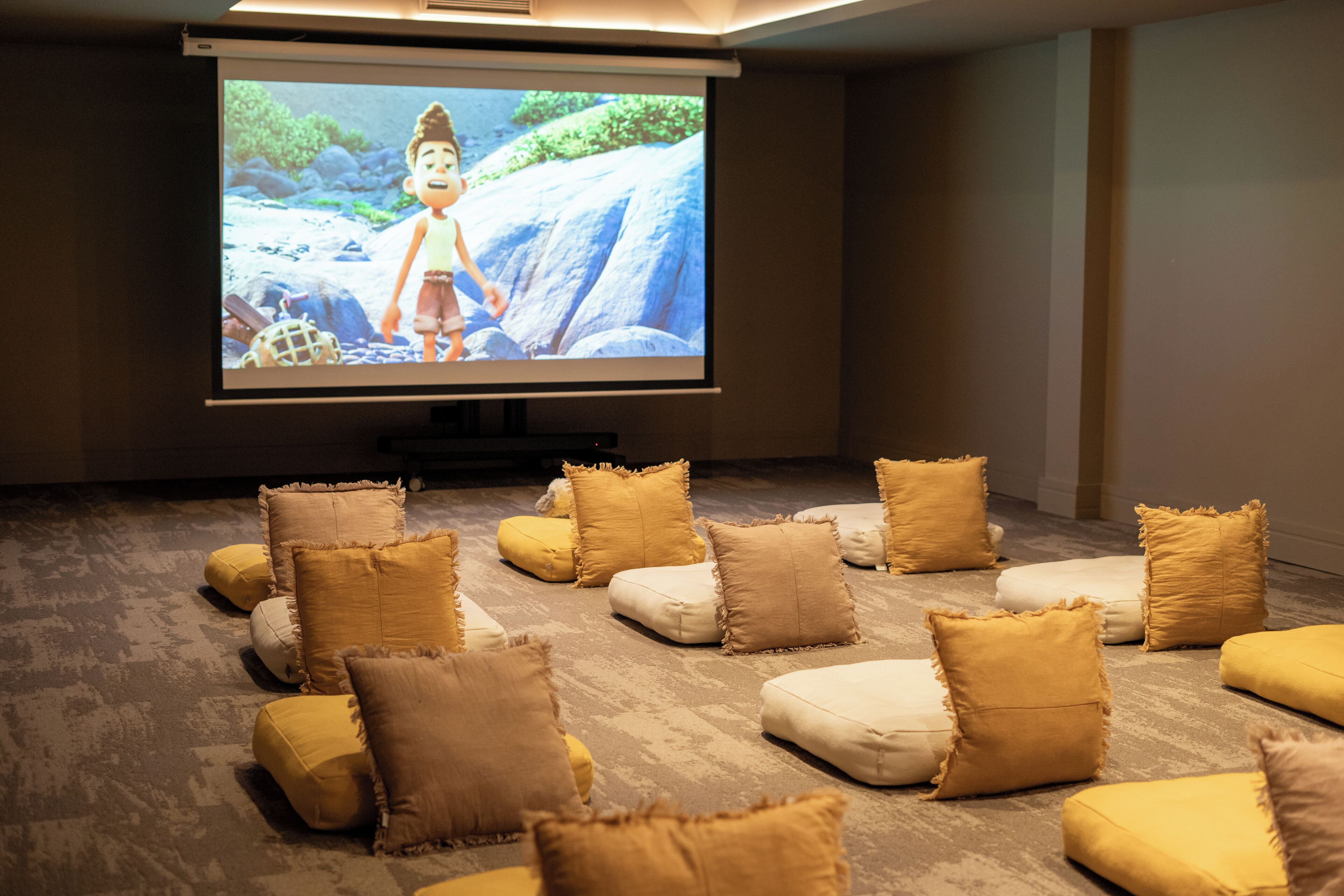 A movie theater with a large screen, cushioned seating, and a projector.