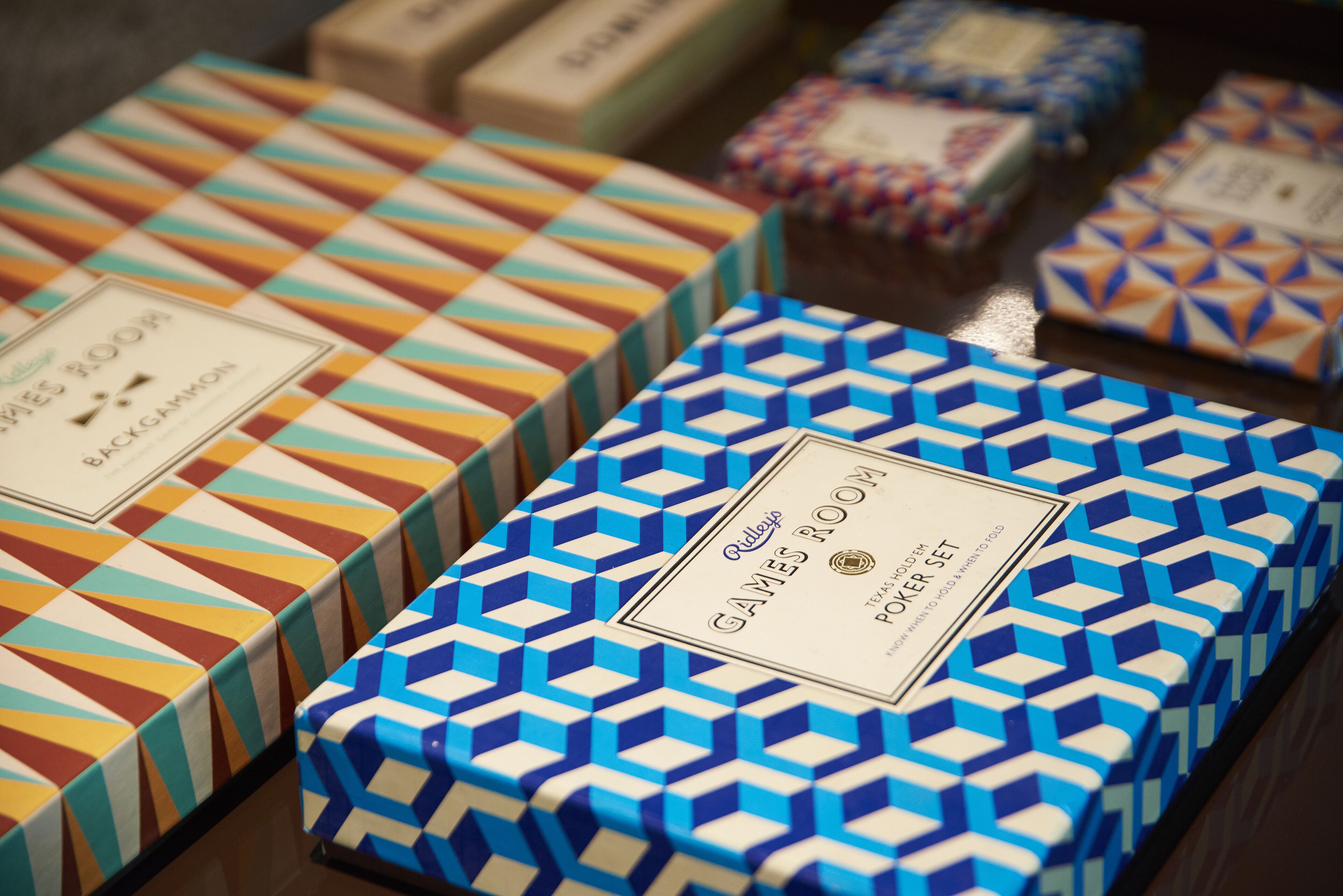 A display of neatly arranged boxes with geometric patterns, each labeled with text indicating they are part of a games room poker set.