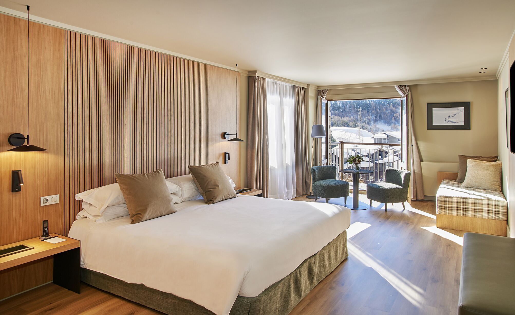 Habitación de hotel con una cama grande, un balcón con mesa y sillas, y vistas al exterior.