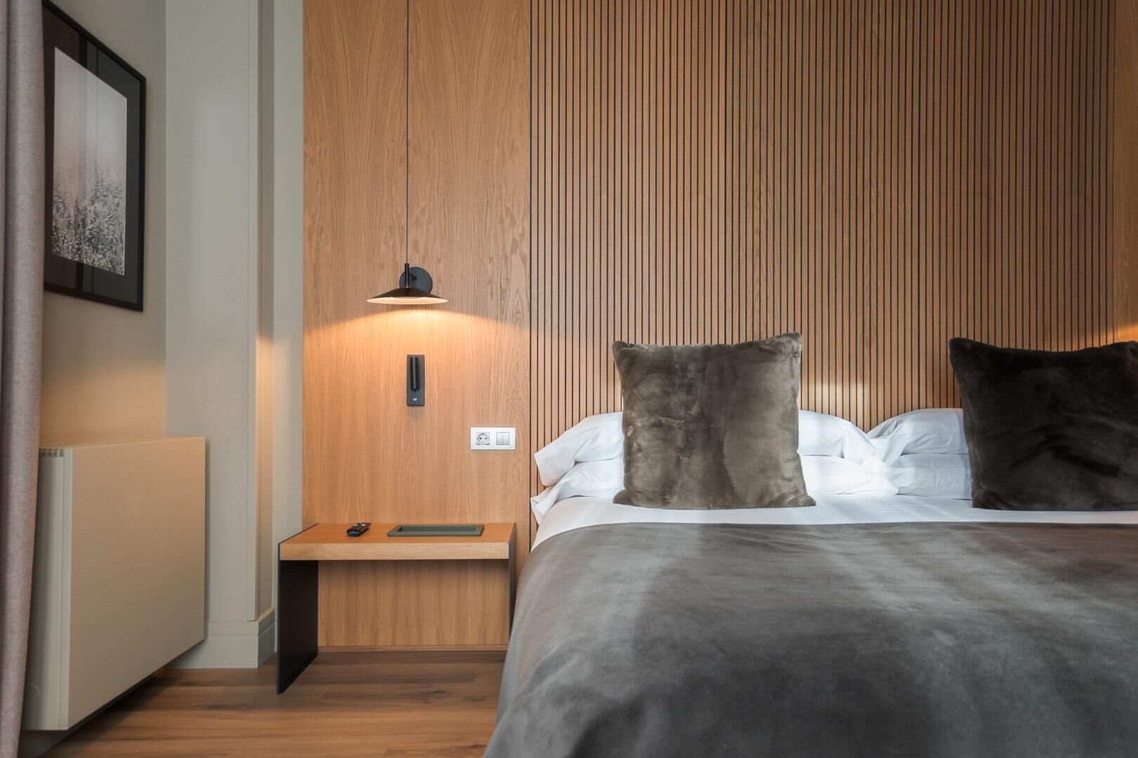 A modern bedroom with a wooden panel wall, a bedside table with a lamp, and a bed with two pillows.