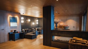 A modern interior with a wooden floor, a seating area with cushions, a wall-mounted light fixture, and a large vase with flowers. - Serras Andorra (Soldeu)