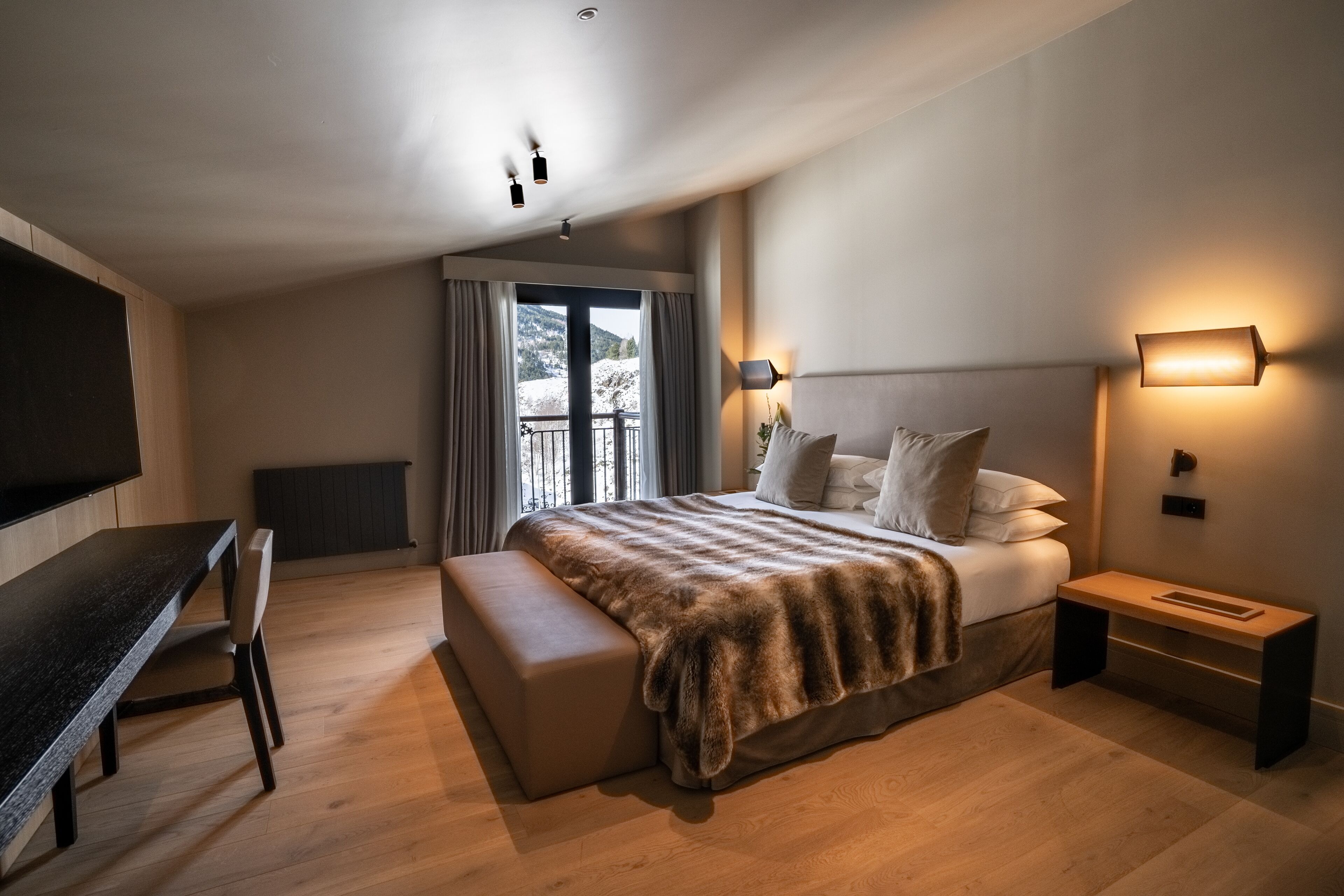 A modern bedroom with a large bed, a desk, and a balcony with curtains.