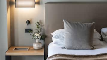 A neatly made bed with a large pillow, a bedside table with a vase of flowers, and a wall-mounted light fixture.