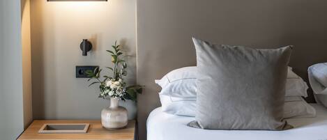 A neatly made bed with a large pillow, a bedside table with a vase of flowers, and a wall-mounted light fixture.