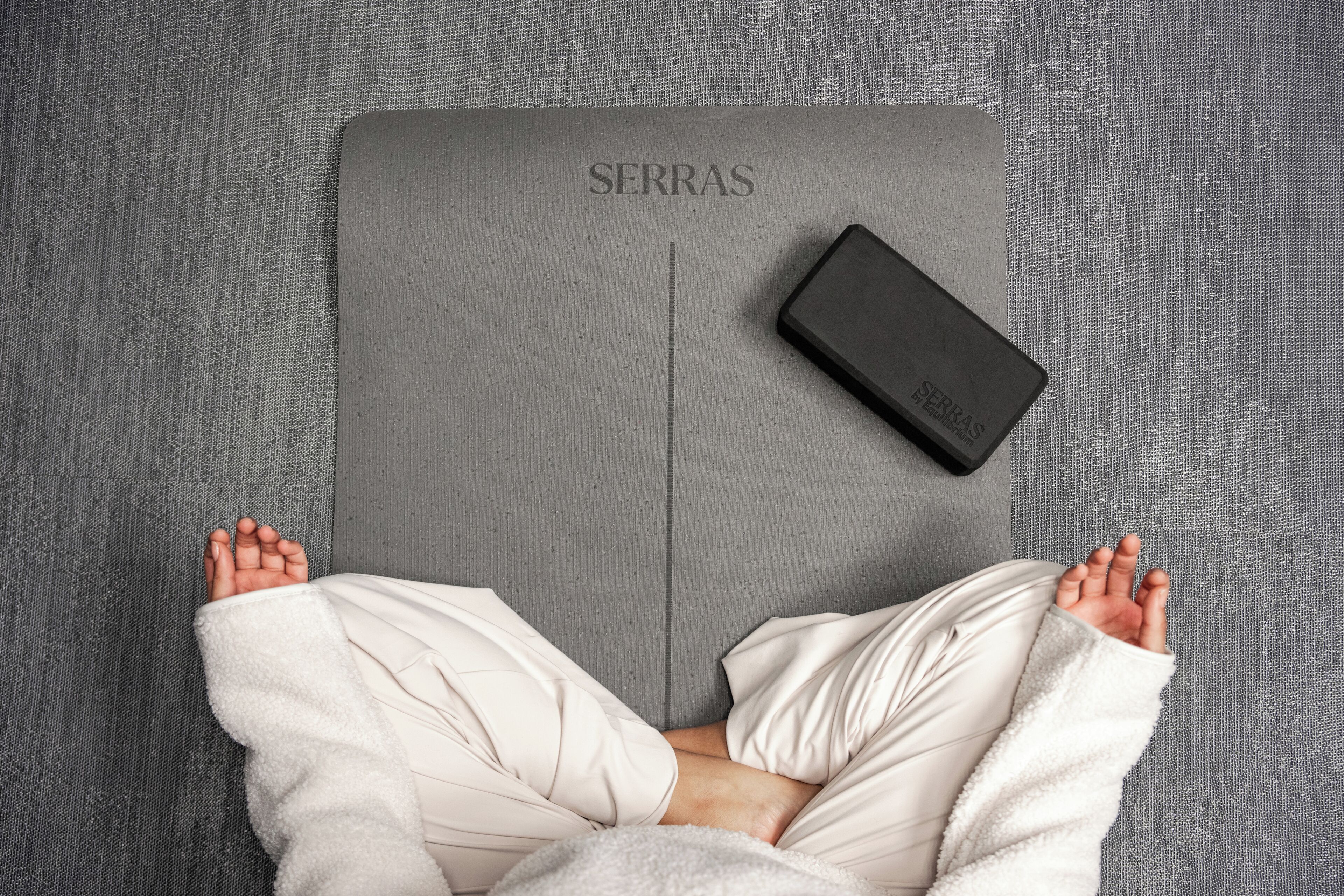 A person lying on a bed with a gray mattress labeled "SERRAS" and a black object beside them.