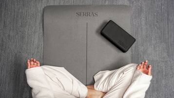 A person lying on a bed with a gray mattress labeled "SERRAS" and a black object beside them.