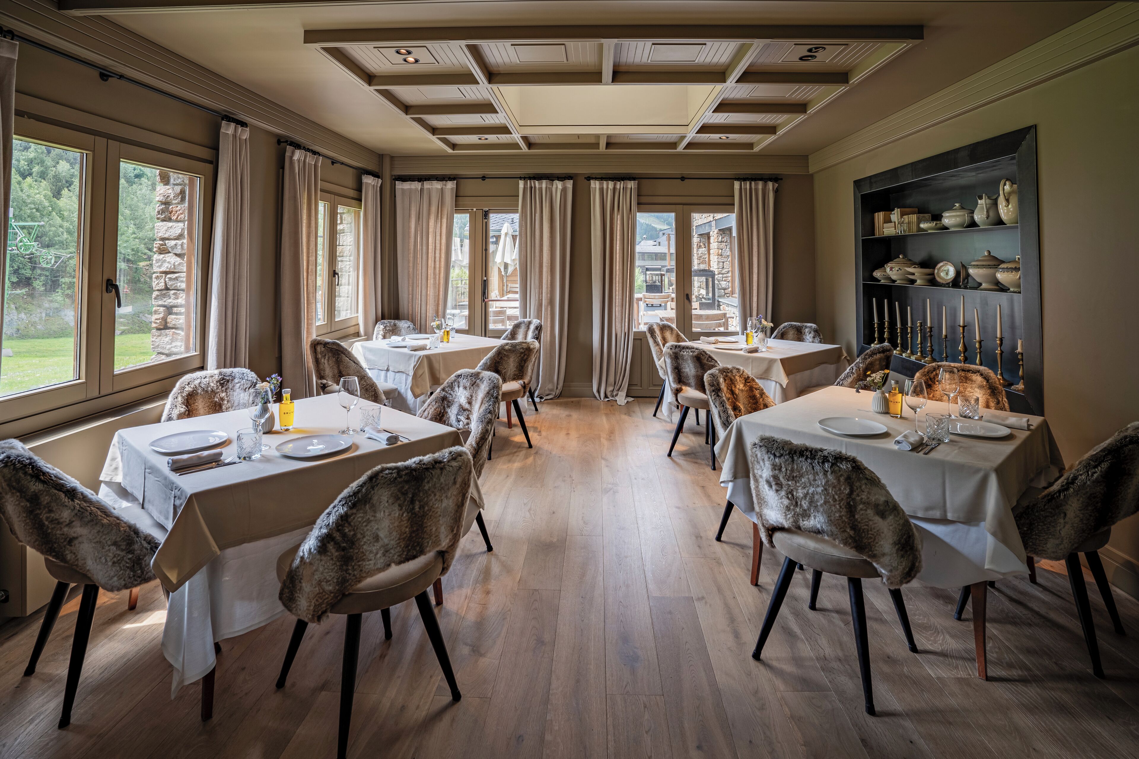 Un comedor con mesas dispuestas para cuatro, cada una con mantel blanco y sillas de piel.