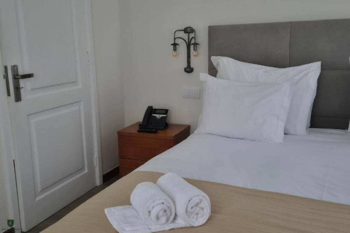 A hotel room with a bed, a bedside table with a phone, and a wall-mounted lamp.