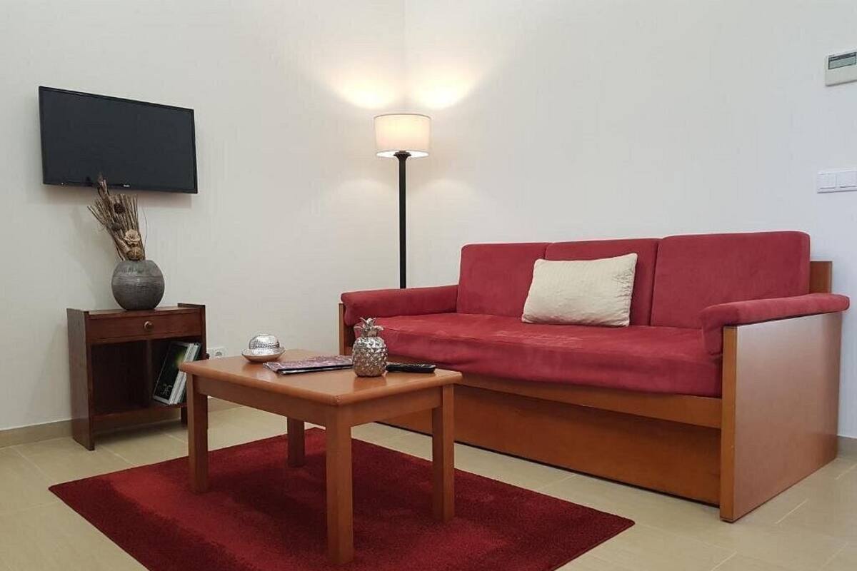 A living room with a red sofa, a wooden coffee table, a lamp, a TV, and a small cabinet.