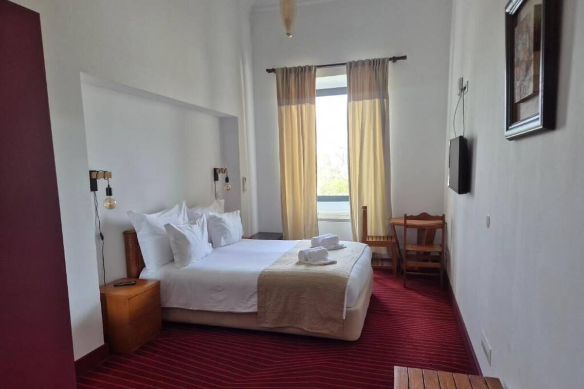 A hotel room with a bed, bedside table, lamp, chair, and a window with curtains.