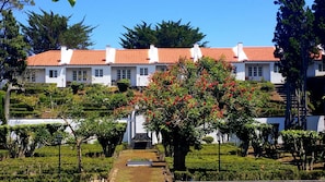 A white building with a red-tiled roof, surrounded by a well-maintained garden with various plants and a central tree with red flowers. - Hotel Solar do Conde (Ponta Delgada)