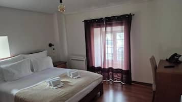 A hotel room with a bed, a desk, a chair, a lamp, and a window with curtains.