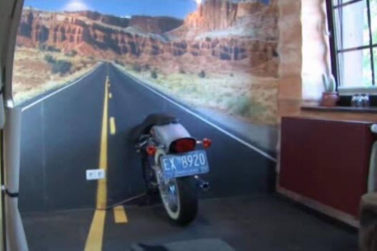 Uma motocicleta estacionada dentro de um veículo com um mural de uma estrada no deserto na parede.