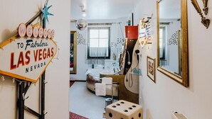 A hallway with a 'Welcome to Fabulous Las Vegas Nevada' sign, a mirror, a red patterned carpet, and a room with a bathtub and a guitar. - Road Stop Motel Dortmund (Dortmund)