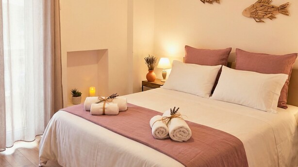 A neatly made bed with a pink and white bedspread, two decorative fish wall art pieces, a bedside lamp, and a wall-mounted air conditioner. - Melo Accommodations (Bari)