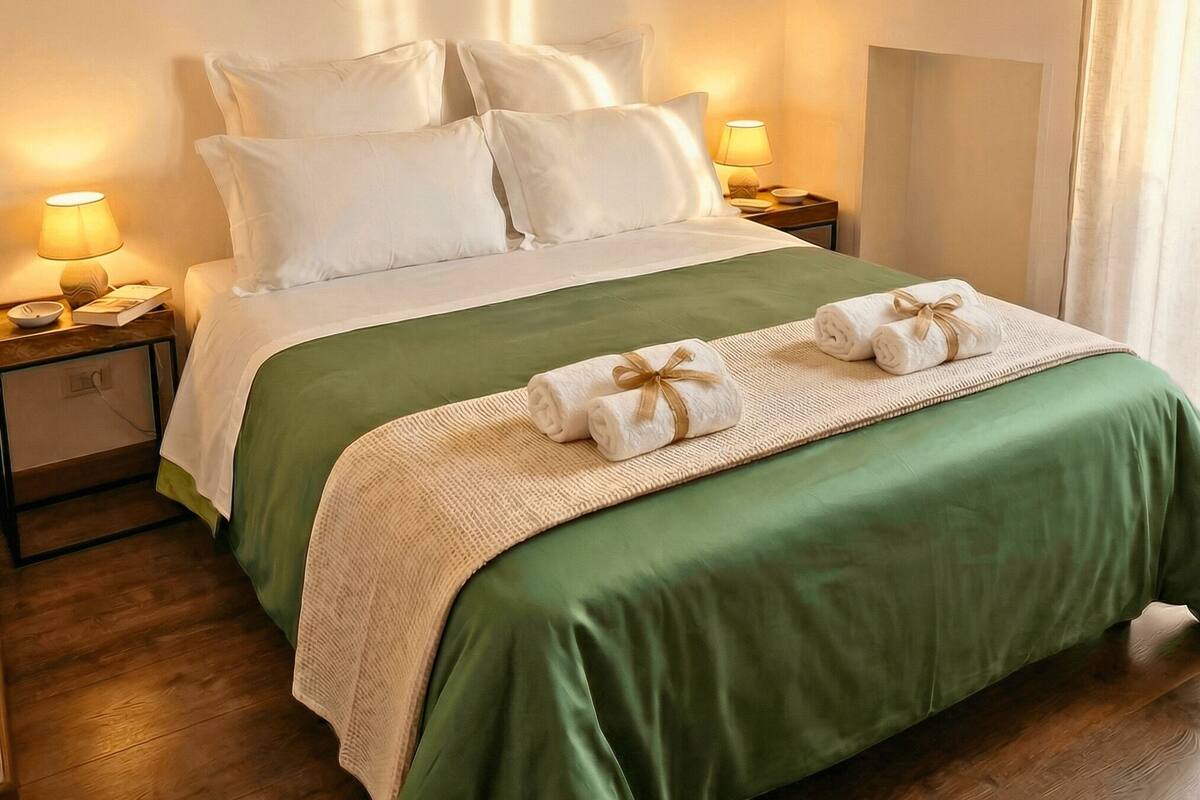 A neatly made bed with a green bedspread, white pillows, and heart-shaped wall decorations.