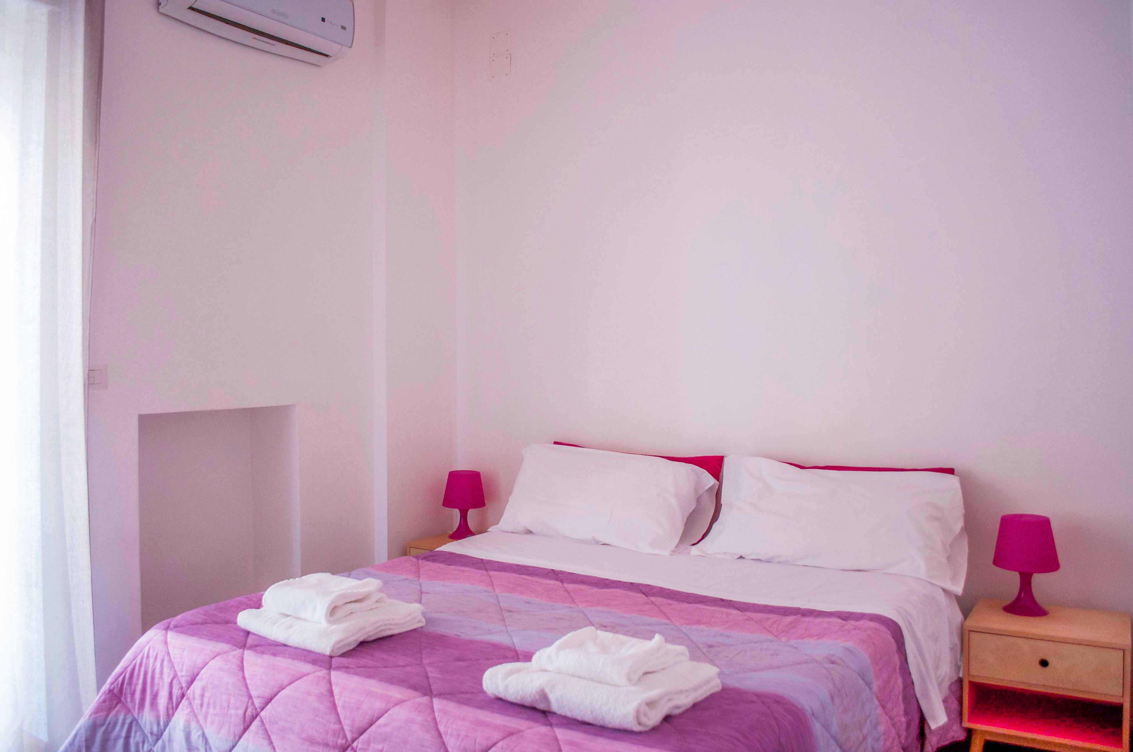 Un lit simple avec une couette rose et violette, deux oreillers blancs et deux lampes de chevet roses.