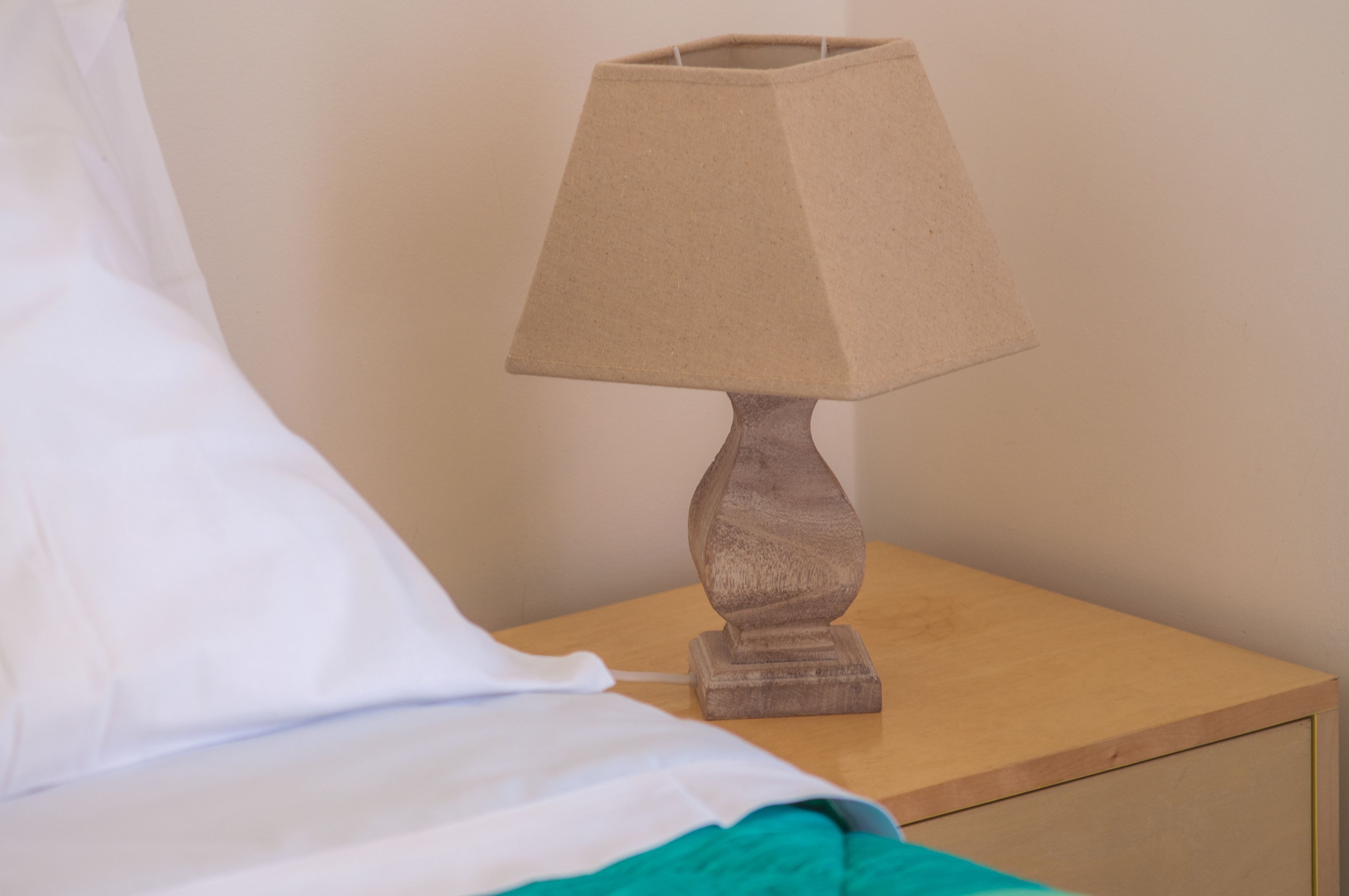 Une table de chevet en bois, avec une lampe et un oreiller blanc.