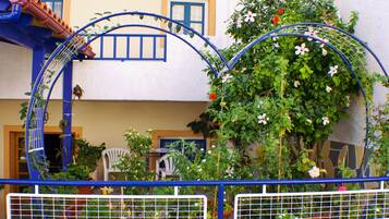 Une cour avec une arche en métal bleue, des plantes en pot et une chaise blanche.